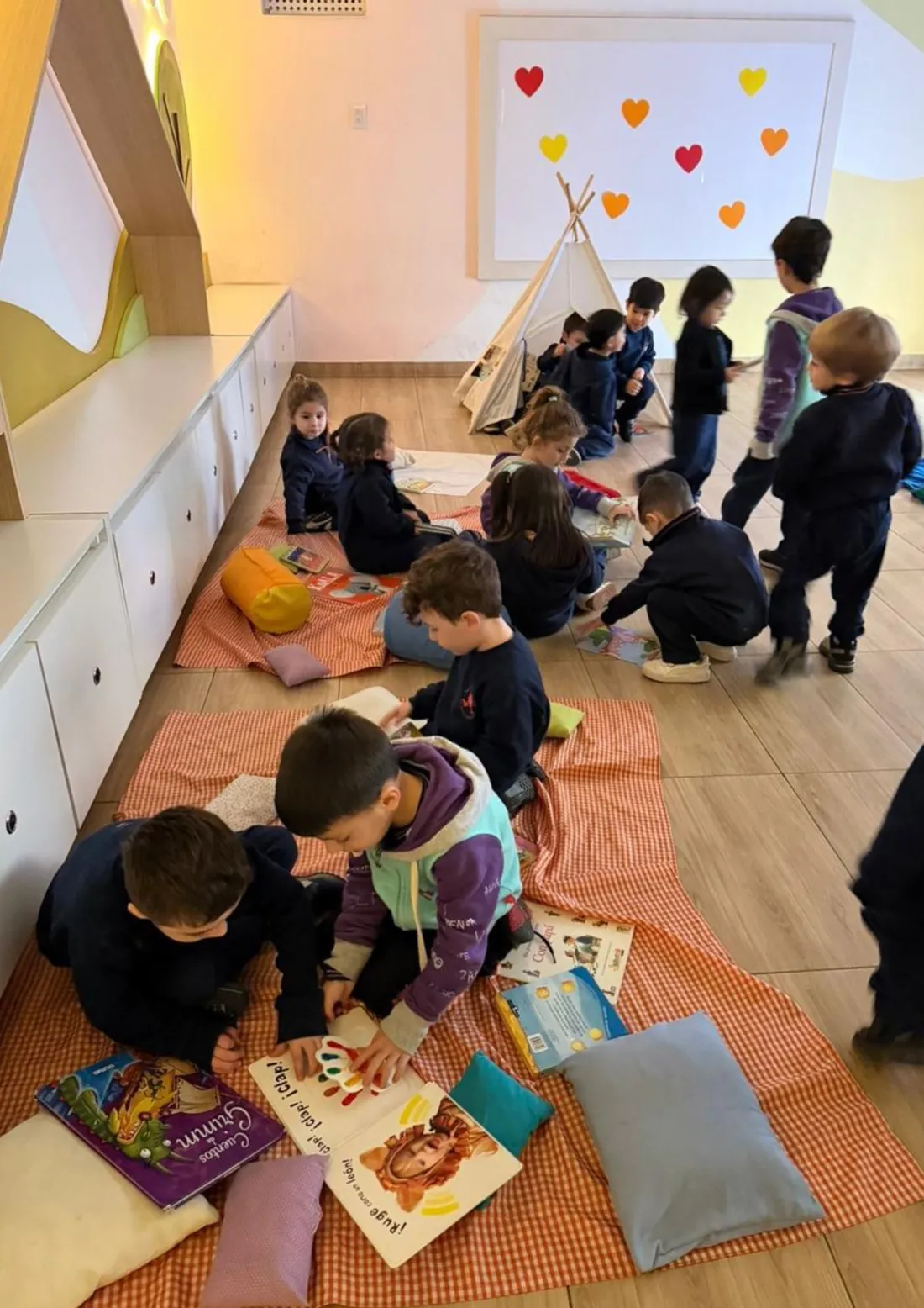 Niños de nivel inicial leyendo sobre mantas en el rincón de lectura de la sala