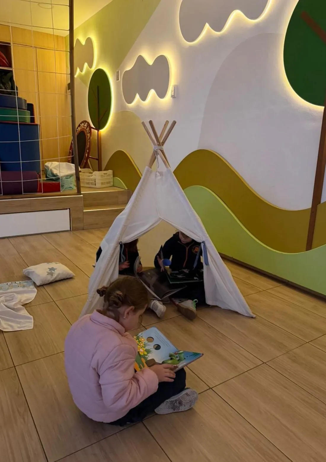 Niñas y niños jugando y leyendo junto a la carpa de la sala del jardín