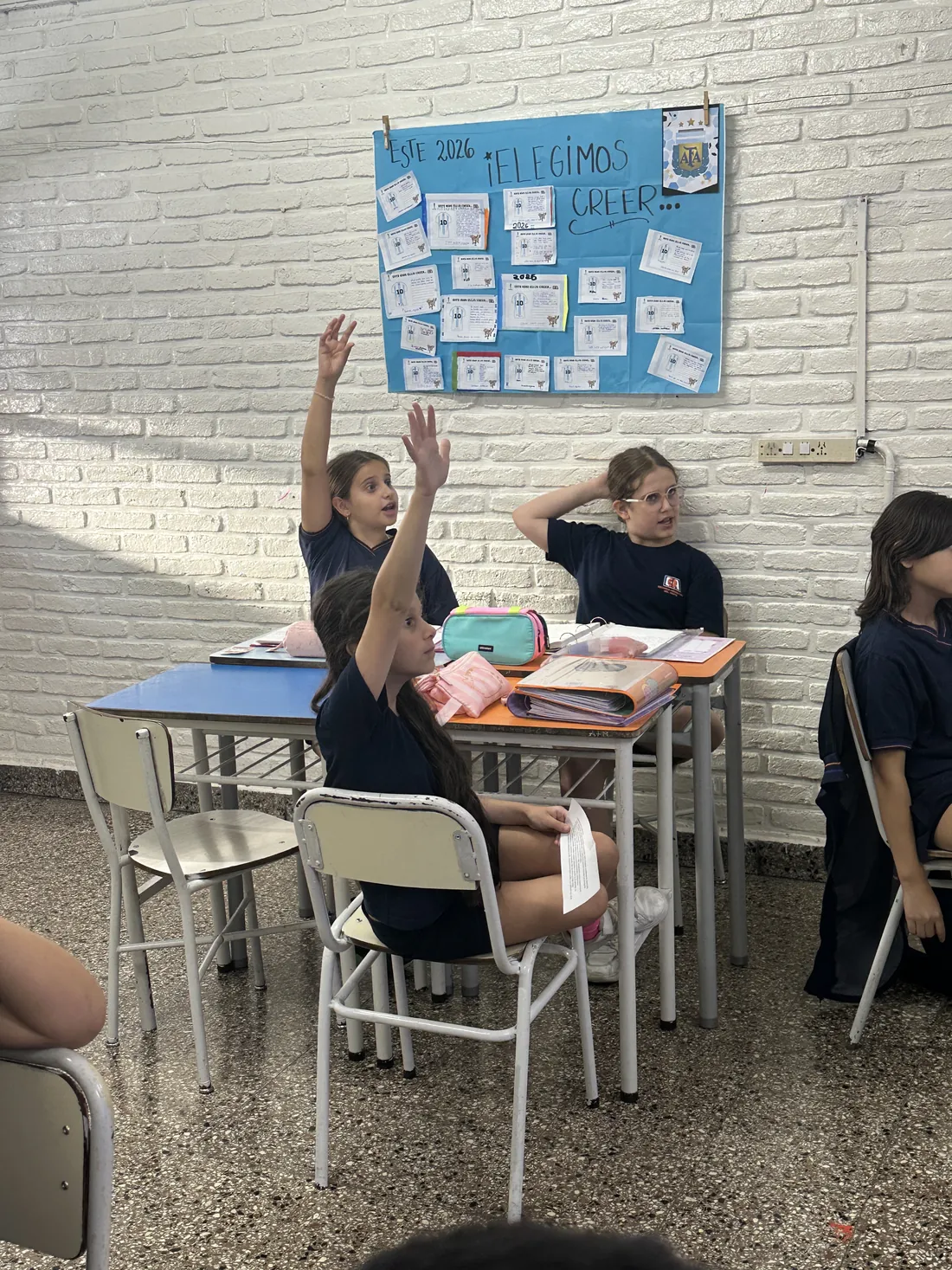 Alumnas de primaria levantando la mano para participar durante la clase