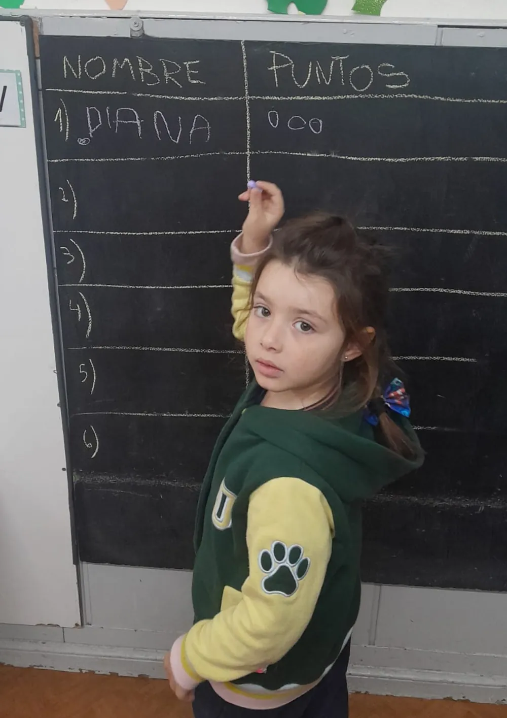 Niña del jardín anotando puntos con tiza en el pizarrón de la sala